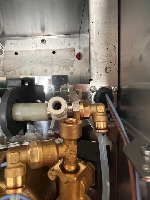 White tee fitting screwed onto the OLAB pump outlet, with the original PTFE tube reconnected on the straight outlet (toward the boiler)